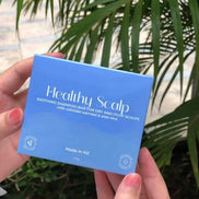 Hand holding a blue box labeled 'Healthy Scalp' with green foliage in the background